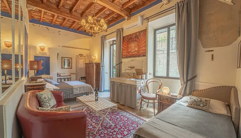 Chambre d'hôte toscane avec lits jumeaux, canapé rouge, tapis persan et plafond en bois sculpté.