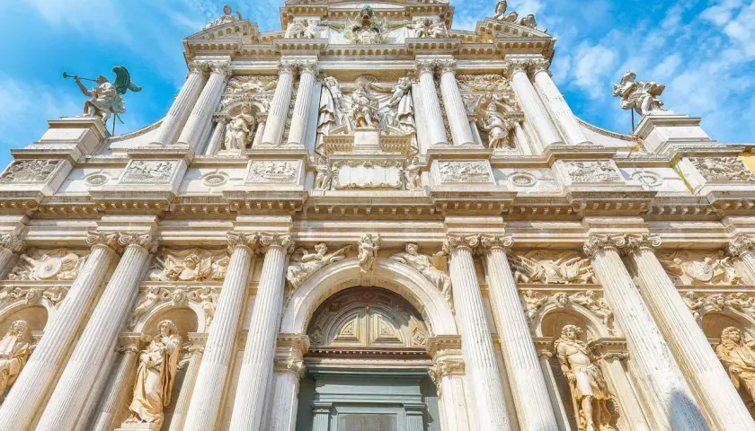 Façade baroque de Santa Maria del Giglio à Venise, ornée de statues et de colonnes imposantes sous un ciel bleu.
