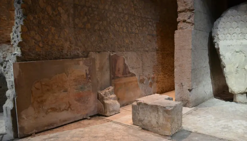 Vestiges d'une fresque murale dans la maison d'Auguste à Rome, avec des blocs de pierre et des murs en ruine.