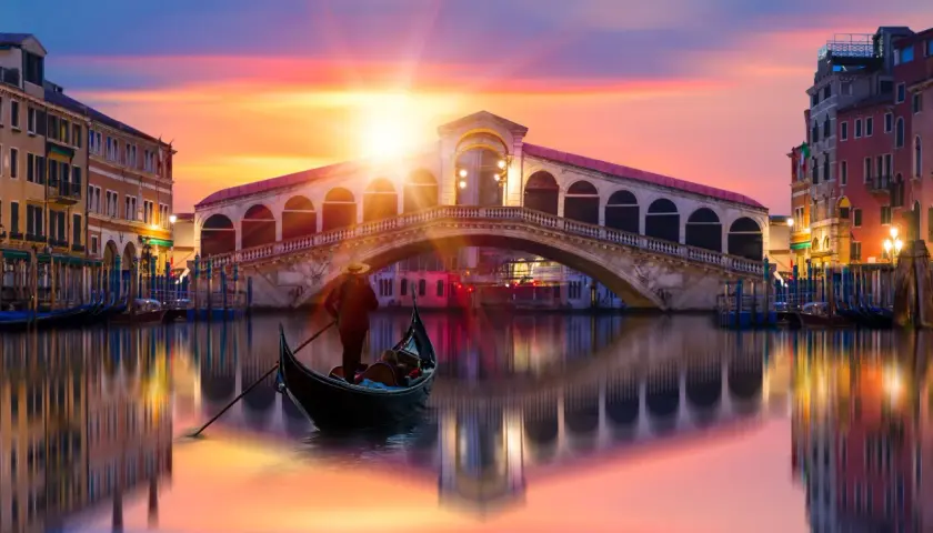 Gondole glissant sur le Grand Canal, sous un ciel aux couleurs vibrantes, avec le célèbre pont du Rialto en arrière-plan. Une scène qui évoque une célèbre peinture de Venise.