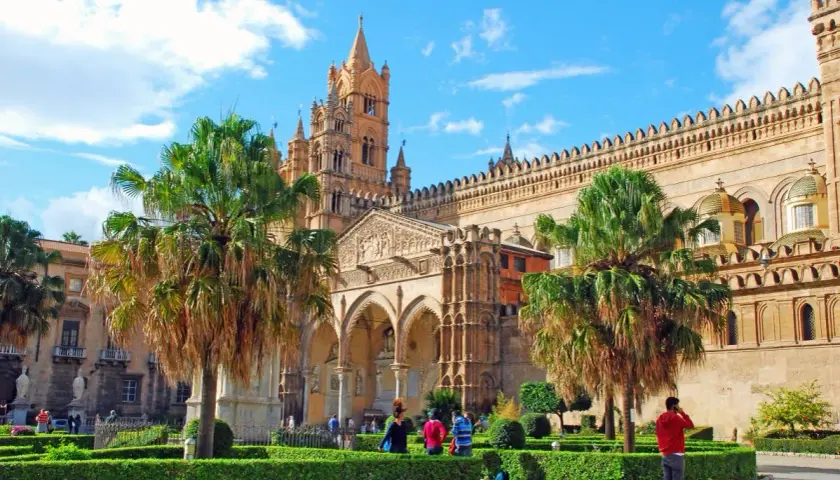 La cathédrale de Palerme, capitale Sicile, se dresse fièrement sous un ciel bleu, entourée de palmiers et de jardins verdoyants.