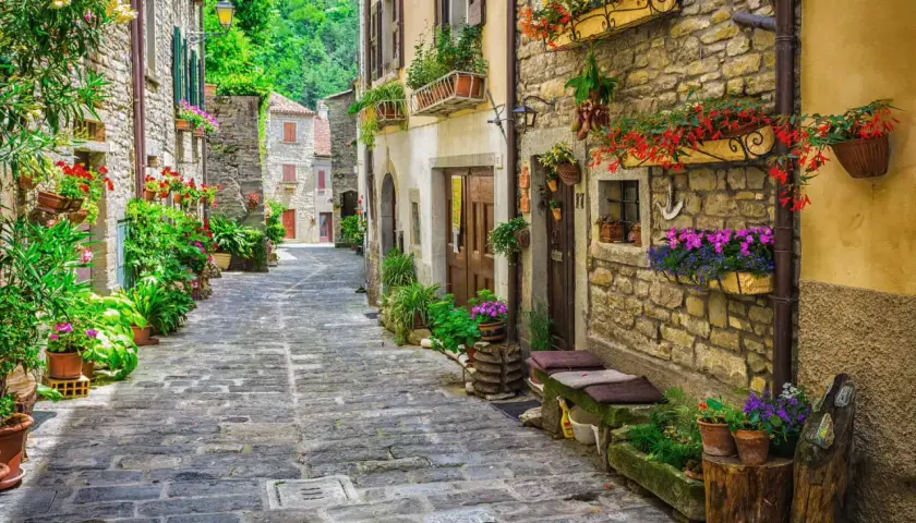 Ruelle pavée bordée de maisons en pierre ornées de fleurs colorées, évoquant une charmante résidence toscane.