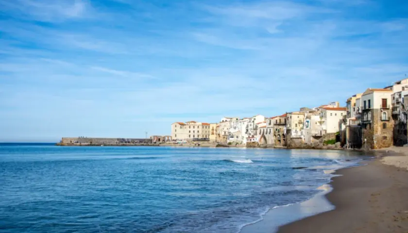 Vue de la plage et des maisons colorées de Cefalù, Sicile, sous un ciel bleu clair.