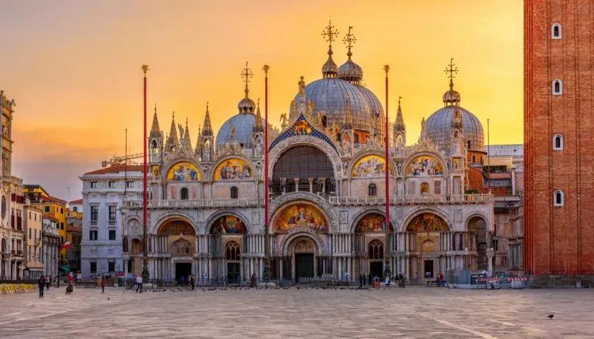 Magnifique coucher de soleil sur la place Saint-Marc, idéal pour visiter la basilique Saint-Marc. La façade ornée de mosaïques brille sous le ciel orangé.