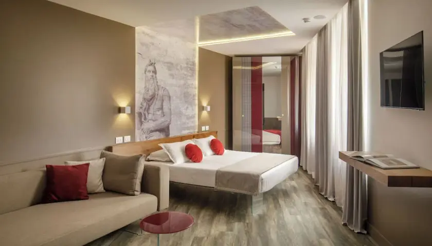 Chambre moderne avec un lit, un canapé et une œuvre d'art murale inspirée de Michel-Ange, typique du **hotel Regno Rome**.