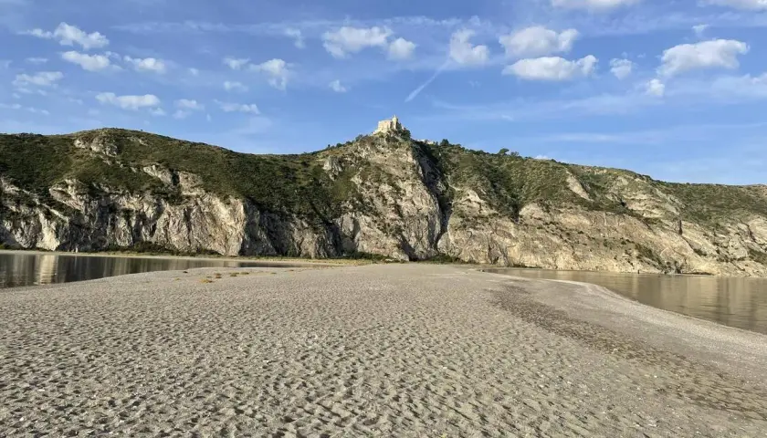 Plage de Patti, Sicile. Un château domine la colline rocheuse surplombant la mer calme et la plage de sable.