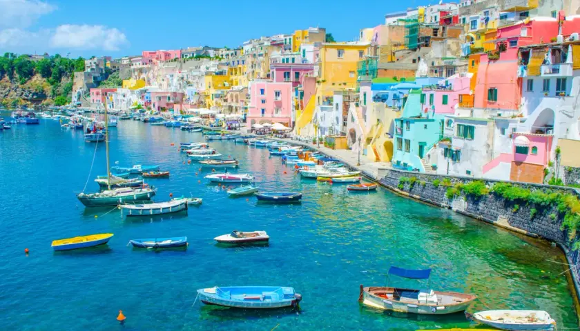 Un charmant port sur une île près de Naples, avec des maisons colorées et de nombreux bateaux dans l'eau turquoise.