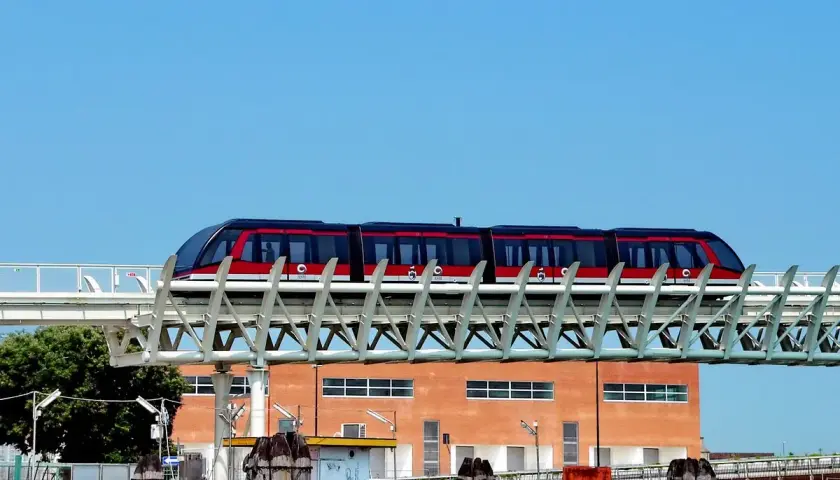 Le people mover de Venise, un train rouge et noir, circule sur une voie aérienne devant un bâtiment orange.