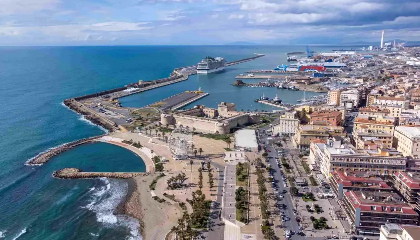 Vue aérienne du port de Civitavecchia, avec un immense paquebot de croisière, des bateaux, une forteresse historique et une grande roue.
