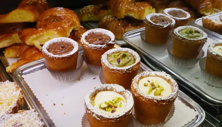 Pâtisseries variées, dont des croissants dorés et des petits gâteaux garnis de crème au chocolat, de pistache ou de crème pâtissière, dans un restaurant florentin.