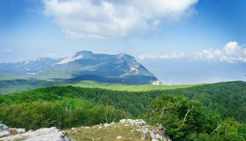 Vue panoramique des montagnes verdoyantes du Cilento, Italie, sous un ciel bleu parsemé de nuages blancs.