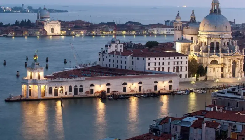 Vue de Venise au crépuscule, avec la basilique Santa Maria della Salute et le bâtiment de la Fondation Pinault Venise illuminés.