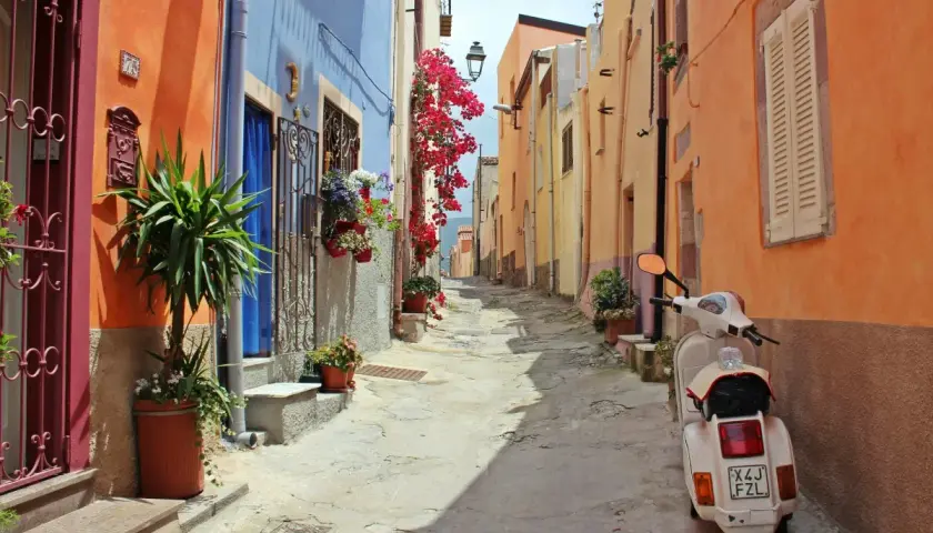 Ruelle colorée en Italie, parfaite pour une location de villa. Un scooter blanc attend, prêt pour l'aventure.