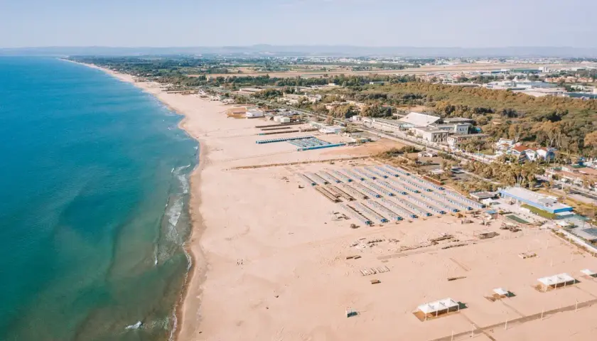 Vue aérienne d'une longue plage de sable fin bordée par la mer bleue, avec des rangées de parasols et des bâtiments à Catane, Sicile.