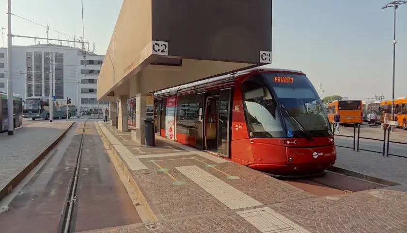 Un tram rouge moderne à Venise, prêt à partir. D'autres bus sont garés à proximité, attendant les passagers.