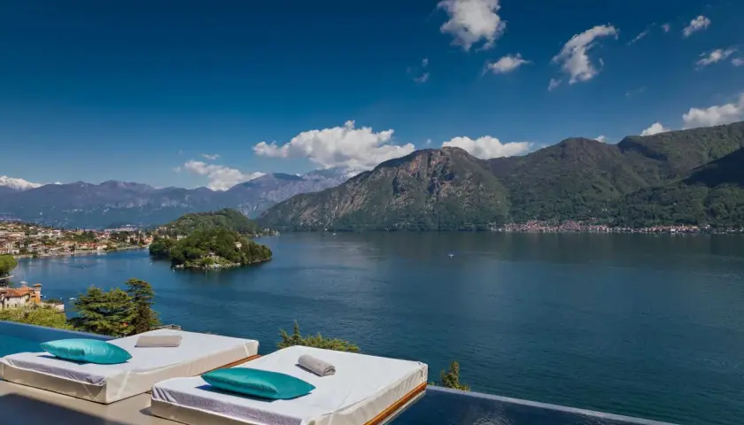 Vue panoramique sur un lac et des montagnes, avec des chaises longues et une piscine à débordement. Idéal pour des gîtes en Italie du Nord.