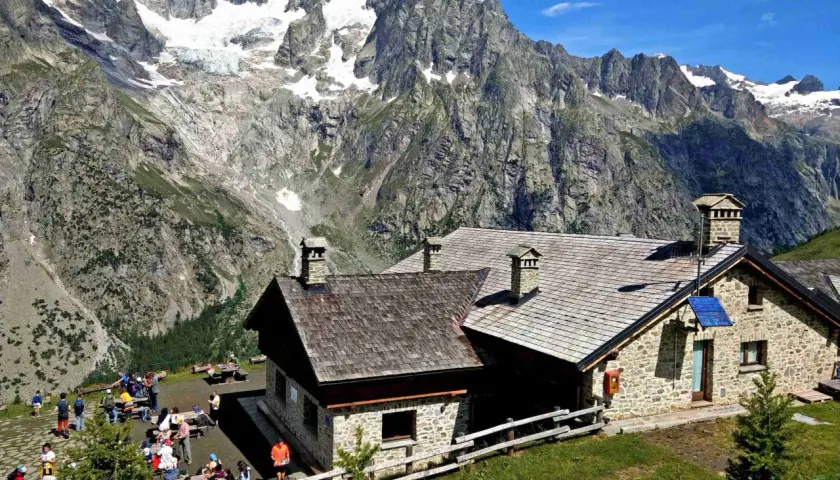 Refuge de montagne en pierre, idéal pour une location vacances Aoste Italie, avec des randonneurs profitant du paysage alpin spectaculaire.