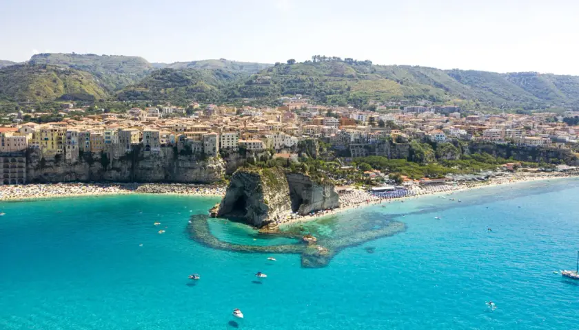 Vue aérienne de Tropea, avec ses maisons colorées perchées sur la falaise, une plage bondée et la mer d'un bleu turquoise éclatant.