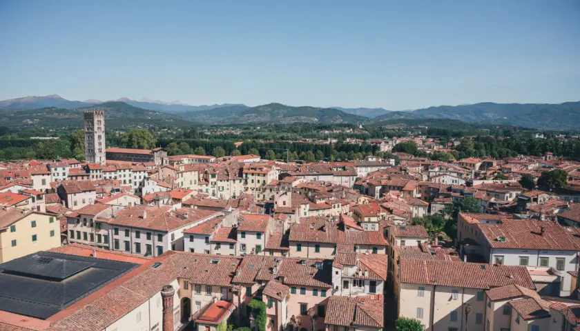 Vue aérienne de Lucques, avec ses toits de tuiles rouges et la tour de Guinigi se détachant sur les collines verdoyantes.