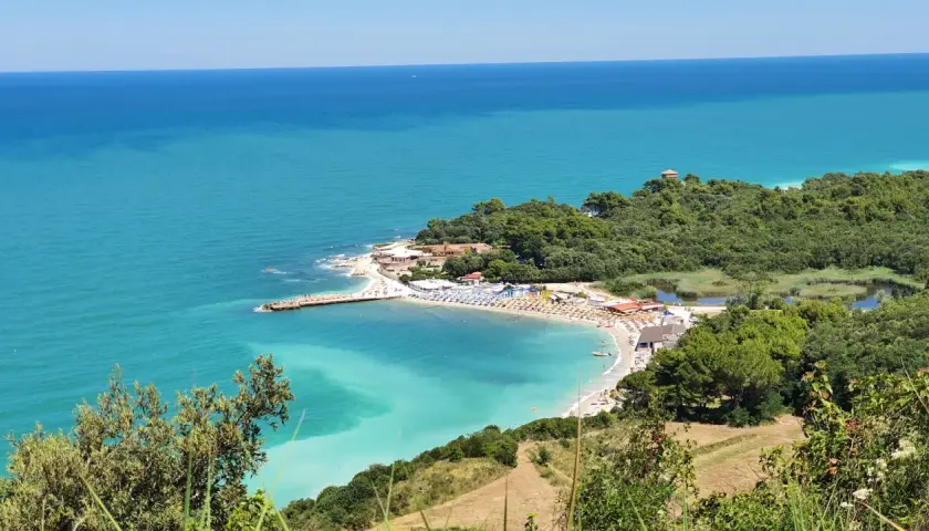 Vue panoramique de la baie de Portonovo, avec ses eaux turquoise, sa plage animée et sa végétation luxuriante.