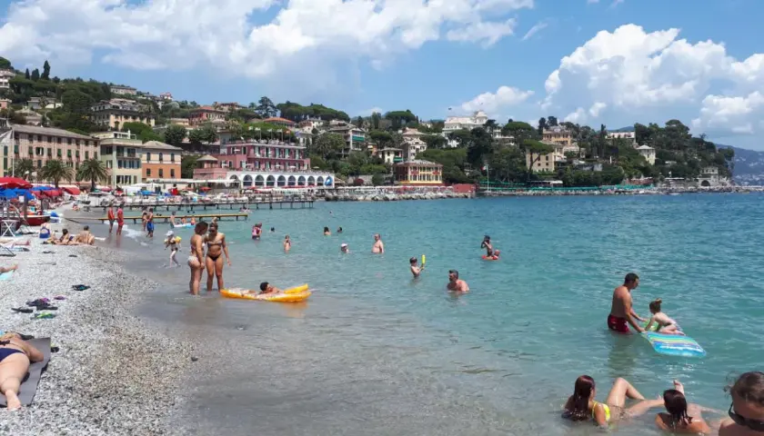 Journée ensoleillée à la plage Santa Margherita Ligure, baigneurs profitant de la mer turquoise et des bâtiments colorés en arrière-plan.