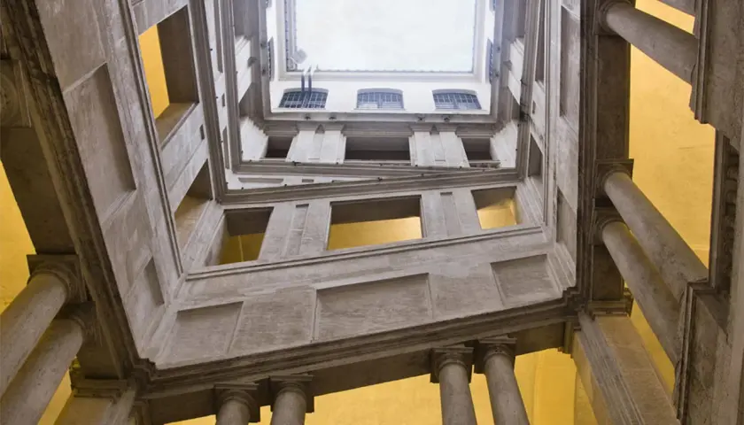 Vue en contre-plongée de l'escalier monumental du Palazzo Barberini, avec ses colonnes imposantes et ses fenêtres lumineuses.
