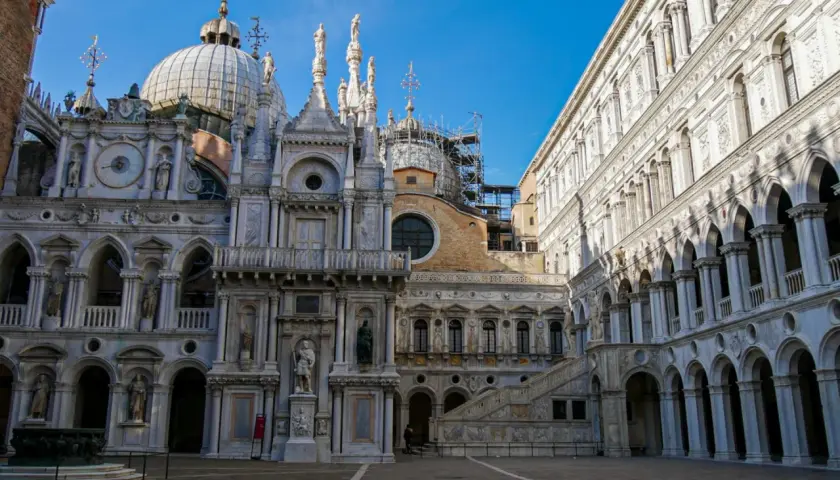 Le **Palais des Doges** à Venise, avec ses dômes, statues et arcades, se dresse majestueusement sous un ciel bleu.