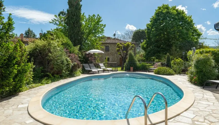 Magnifique piscine dans un jardin luxuriant, typique d'une location en Toscane. Le soleil brille sur l'eau bleue, invitant à la détente.