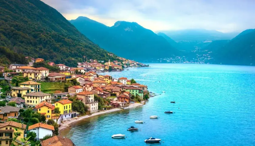 Village coloré au bord d'un lac bleu vif, niché au pied de montagnes verdoyantes. Un paysage typique des 3 lacs en Italie.