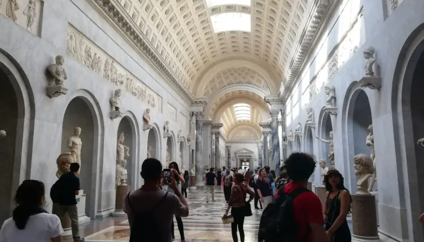 Visiteurs admirant des sculptures dans un long couloir orné de bustes et de bas-reliefs. Une excellente façon de savoir comment aller au Vatican.