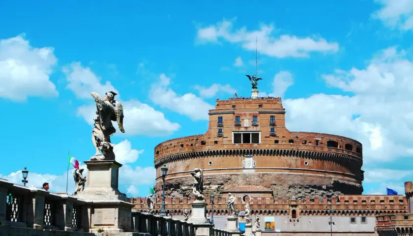 Le **château** Sant'Angelo à **Rome**, avec ses statues d'anges sur le pont, se dresse sous un ciel bleu éclatant.