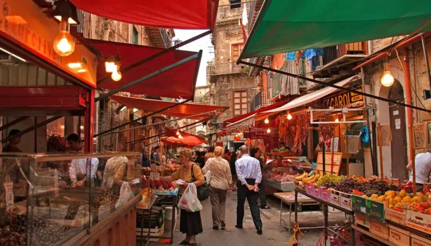 Ambiance animée au marché de la Vucciria à Palerme, avec des étals colorés, des fruits frais et des boucheries.