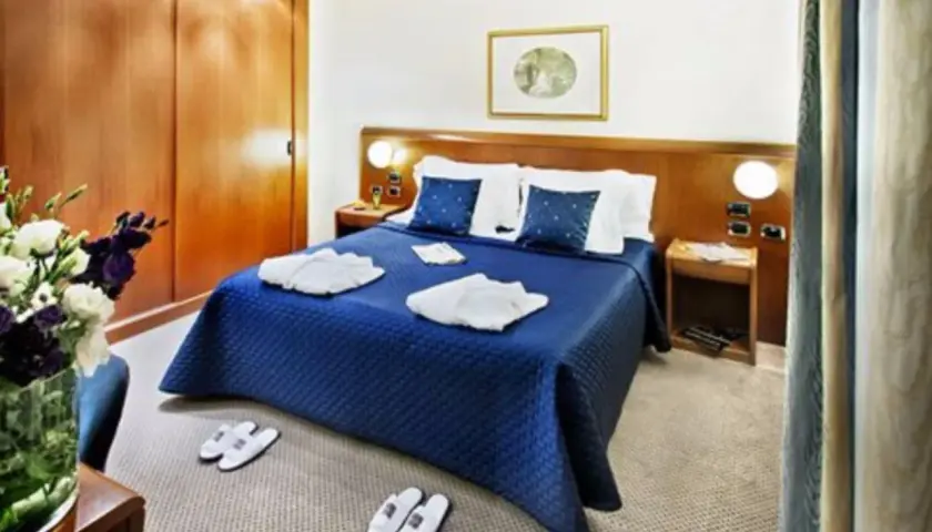 Chambre confortable à l'hôtel Ponte Sisto Rome avec lit bleu, peignoirs et pantoufles.