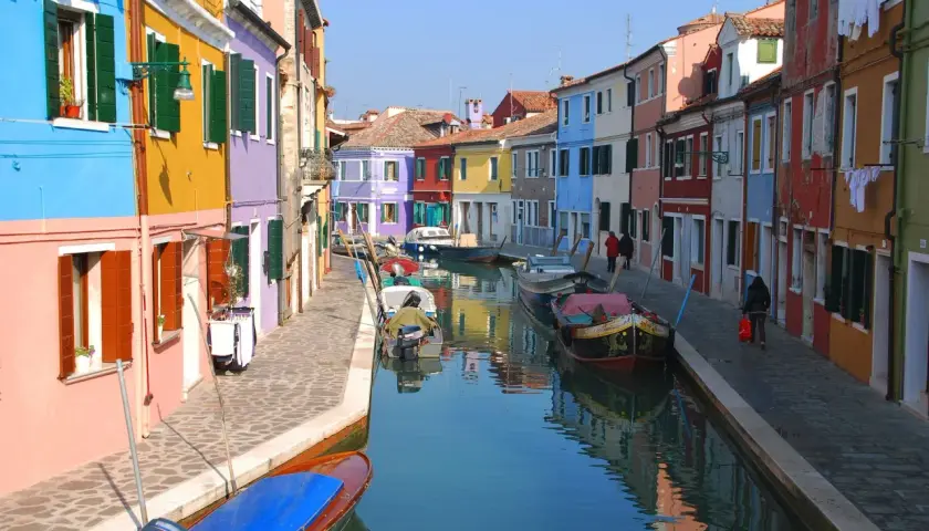 Canal bordé de maisons colorées à Murano, Venise. Des bateaux sont amarrés le long de la voie navigable, reflétant les façades vibrantes.
