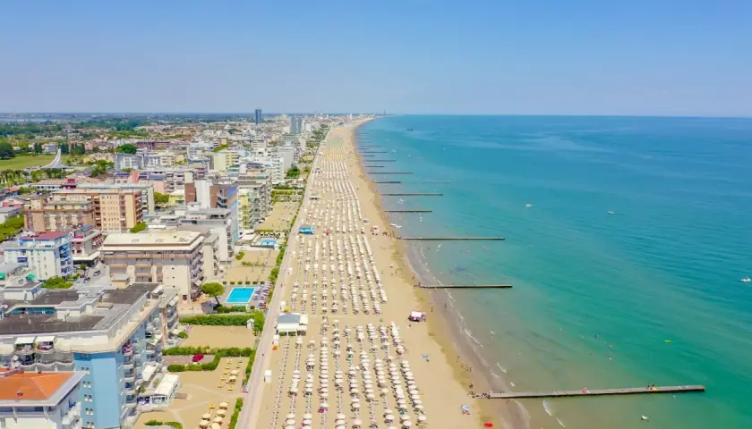Vue aérienne de la longue plage de Lido di Jesolo, avec des rangées de parasols blancs, des hôtels et la mer Adriatique bleue.