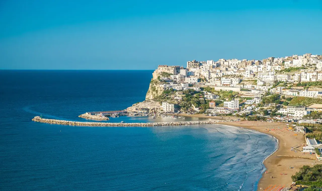 Vue panoramique de Peschici, Italie, avec ses maisons blanches perchées sur la falaise, sa plage de sable fin et son port pittoresque.