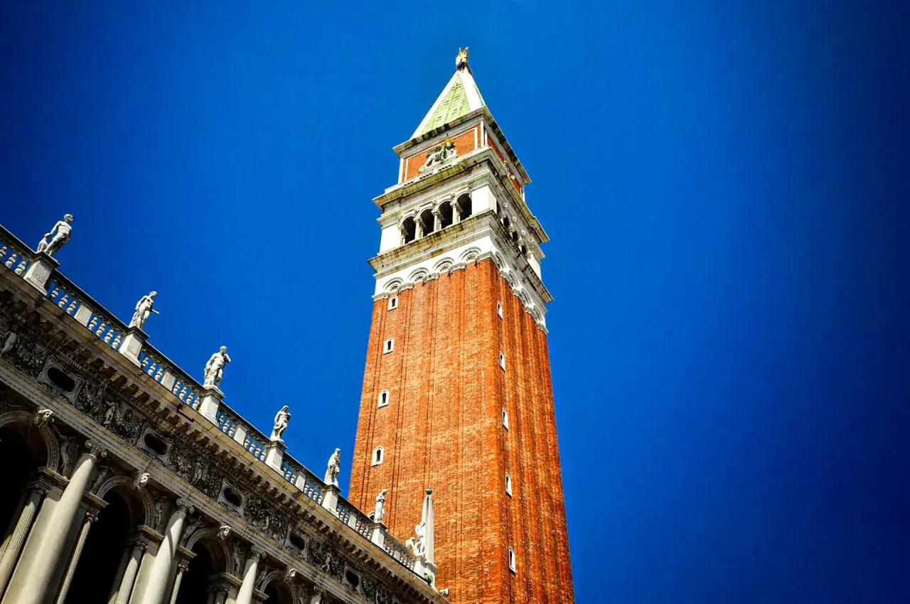 Le campanile de Venise se dresse fièrement sous un ciel bleu éclatant, orné de statues sur son flanc.
