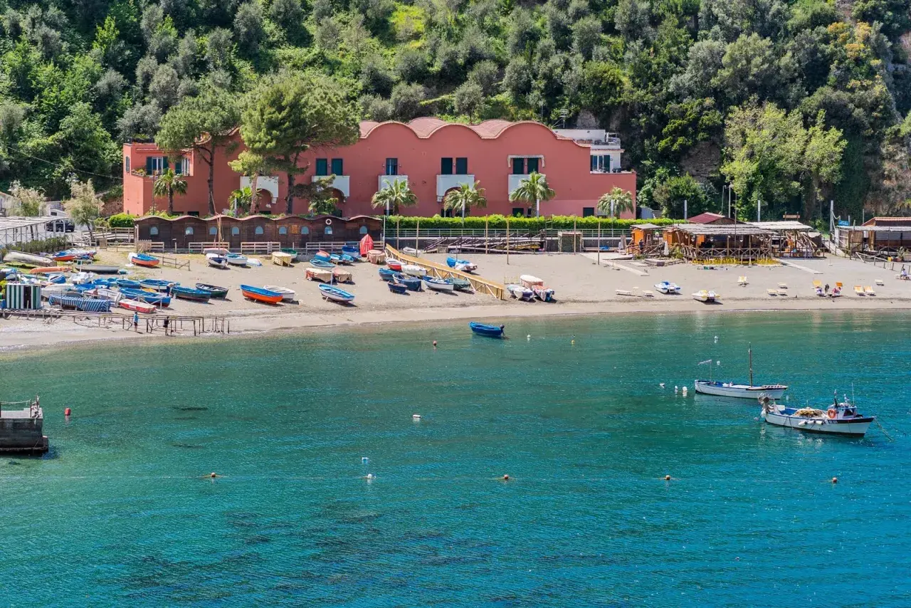 Plage de Vico Equense avec des bateaux colorés sur le sable et dans l'eau turquoise. Bâtiment rose en arrière-plan.