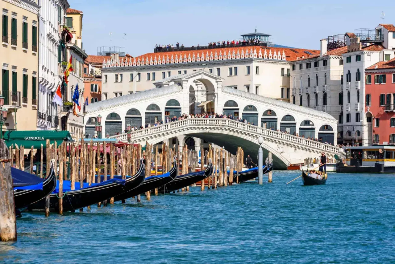 Gondoles amarrées près du célèbre Ponte di Rialto, avec des touristes admirant la vue sur le Grand Canal.