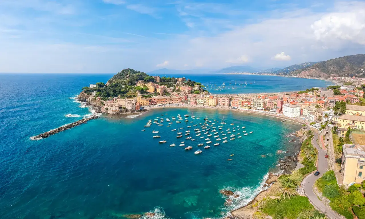 Vue aérienne de la baie de Sestri Levante, avec ses maisons colorées, sa plage et une multitude de bateaux dans les eaux turquoise.