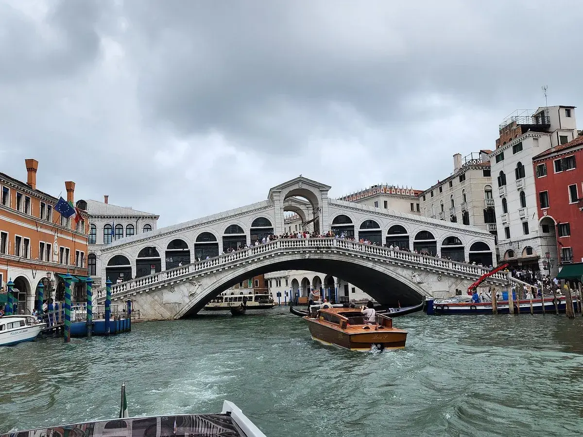Un taxi venise navigue sur le Grand Canal, passant sous le célèbre pont du Rialto, bordé de bâtiments colorés.