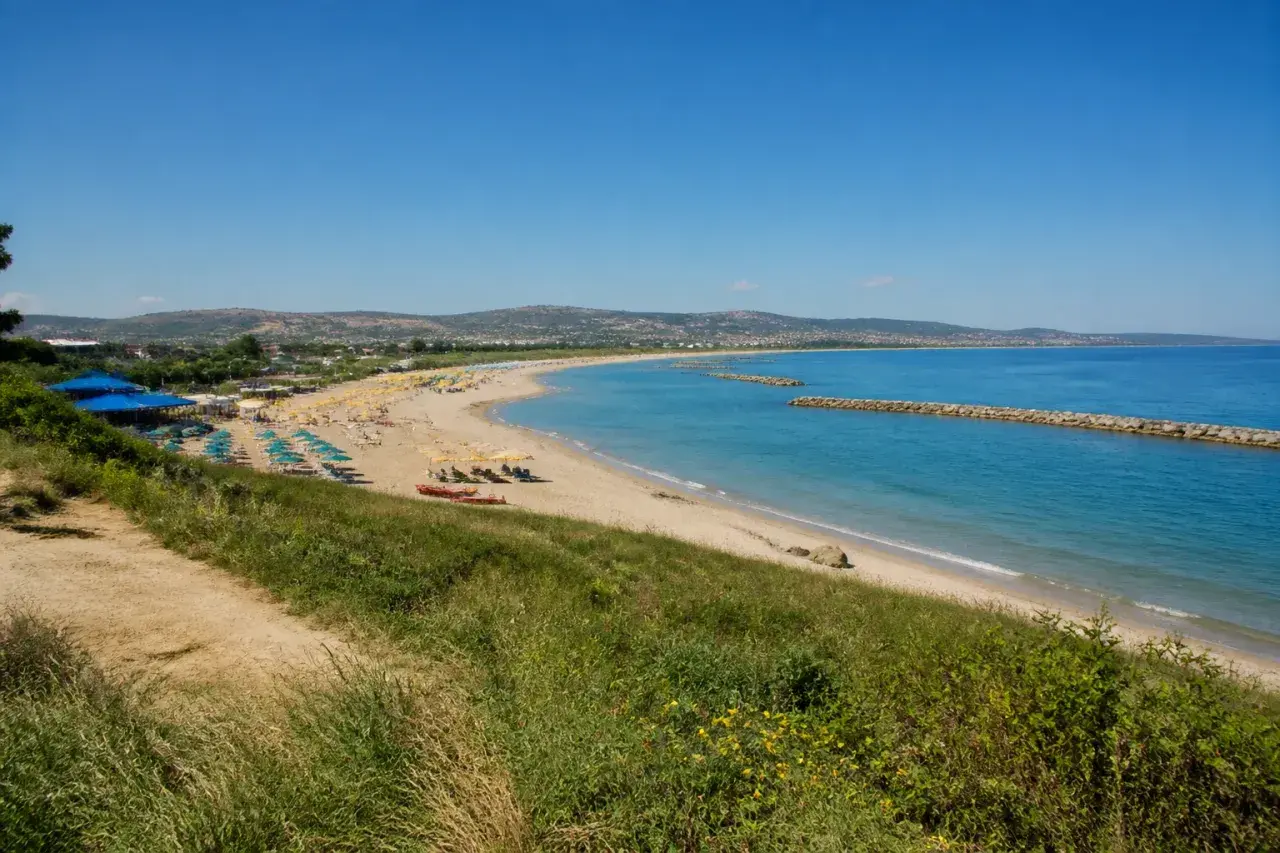 Plage de Pescara, Italie. Parasols bleus et jaunes, mer turquoise, digues en pierre, collines verdoyantes.
