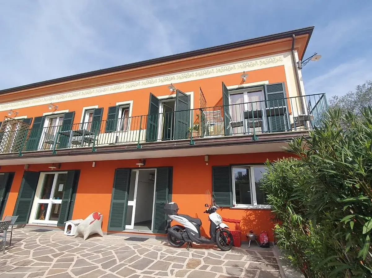 Façade orange vif de l'hôtel Olivium La Spezia avec balcons, volets verts et scooter blanc sur la terrasse pavée.