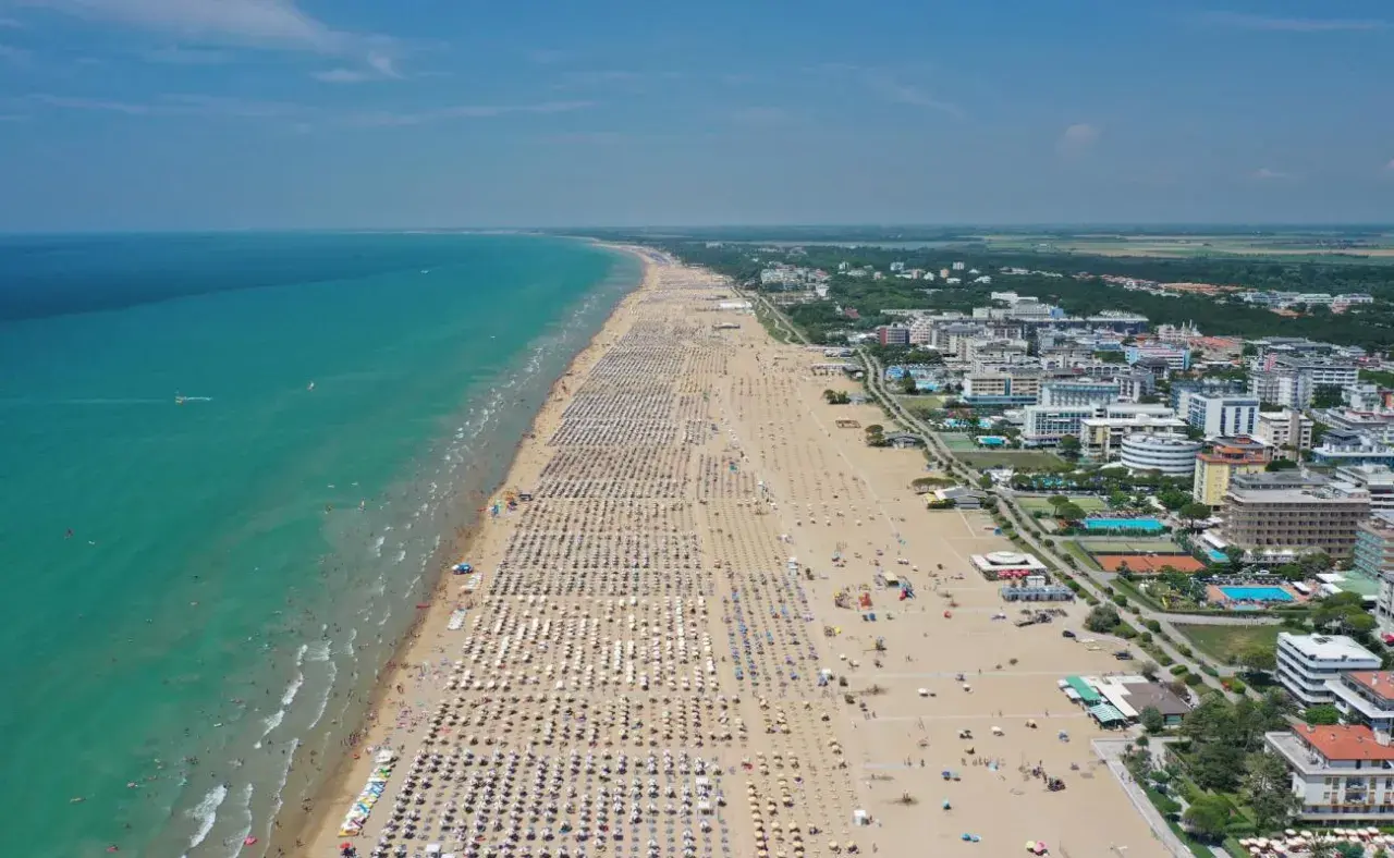 Plage bondée de parasols et de baigneurs à Bibione, Italie, avec la mer turquoise et des hôtels en arrière-plan.