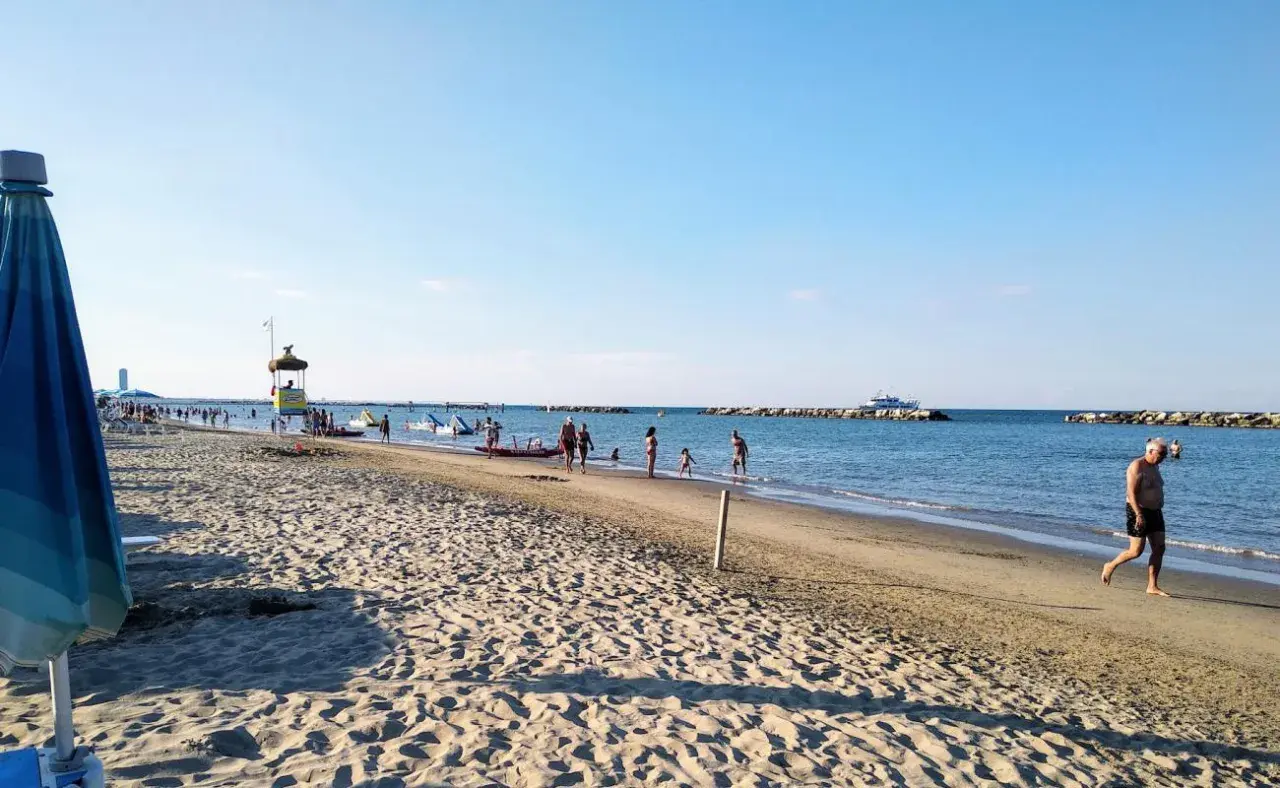 Plage animée à Gatteo Mare, avec des baigneurs, des enfants jouant dans l'eau et un poste de secours. Un bateau navigue au loin.
