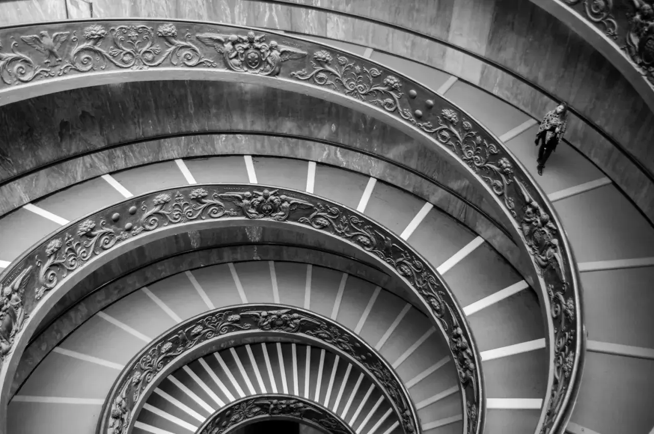 Un escalier en colimaçon orné, rappelant une coupole du Vatican, avec une personne solitaire descendant ses marches.
