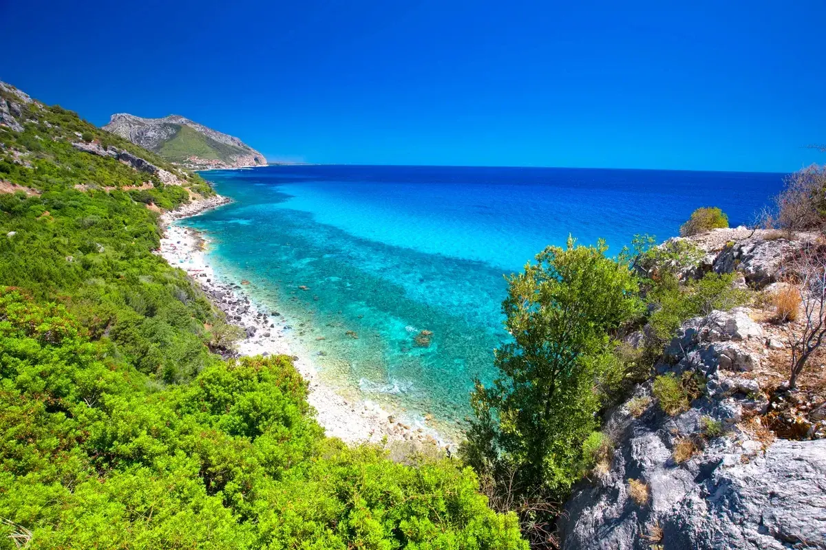 Vue panoramique de la côte de **Sardaigne Cala Gonone**, avec ses eaux turquoise cristallines, sa plage de galets et sa végétation luxuriante.