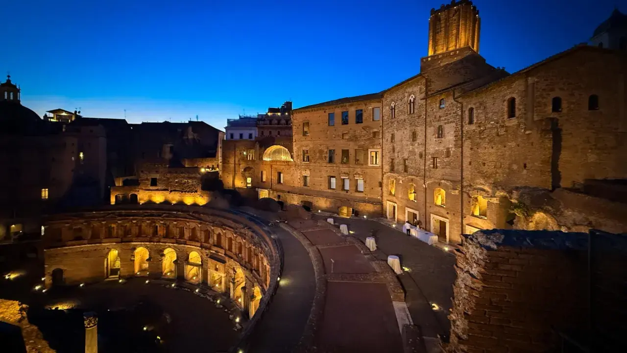 Les marchés de Trajan s'illuminent dans la nuit romaine, vestiges antiques baignés d'une douce lumière dorée sous un ciel bleu profond.