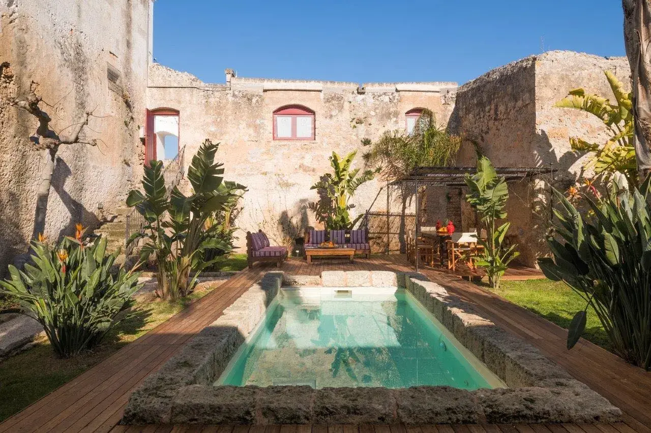 Cour intérieure d'une masseria en Italie, avec piscine, mobilier de jardin et végétation luxuriante.