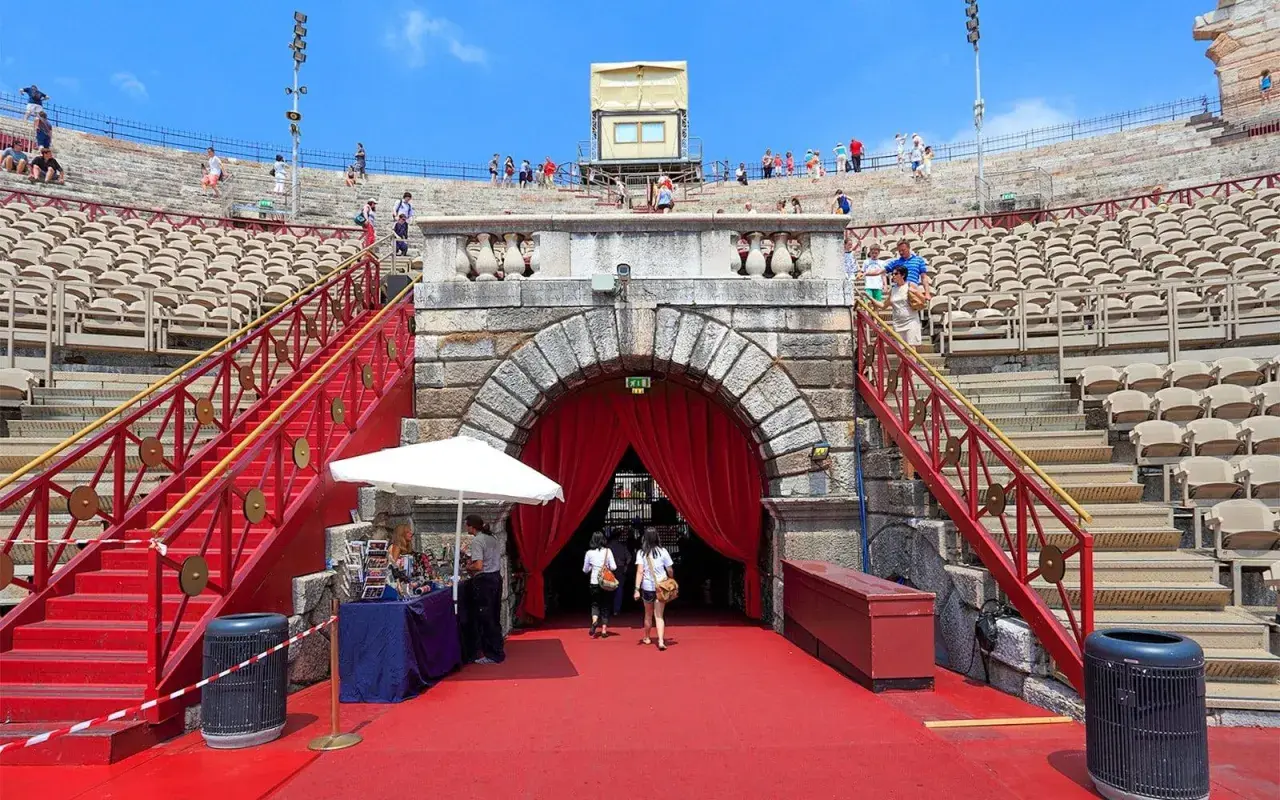 L'Arène de Vérone, avec ses gradins de pierre et ses escaliers rouges, accueille des visiteurs sous un ciel bleu.